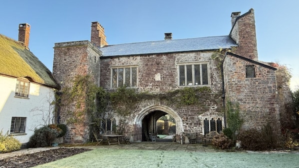 A stone building with a thatched roof, an arched entrance, and a small garden area.