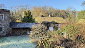 A stone building with a thatched roof, a fenced yard, and a tree in the foreground.