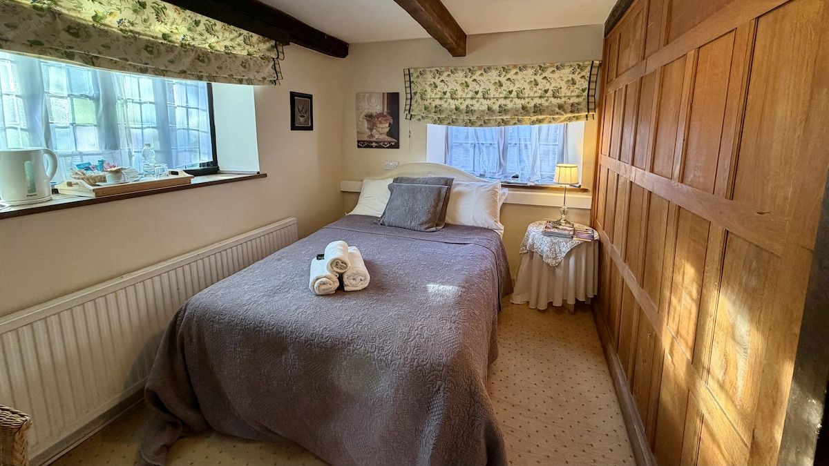 A bedroom with a bed, a window with curtains, a radiator, and a wooden wall.