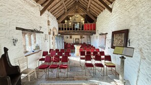 A room with stone walls, wooden beams, and red chairs arranged for seating.