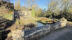 A stone bridge over a canal with a stone wall on one side and trees in the background.