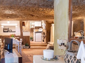 An interior with a rustic stone ceiling, a kitchen area with a sink and cabinets, a dining area with a table and chairs, and a computer setup.