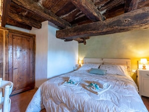 Una camera da letto con soffitto in legno, un letto con lenzuola bianche, un comodino con una lampada e una porta in legno.