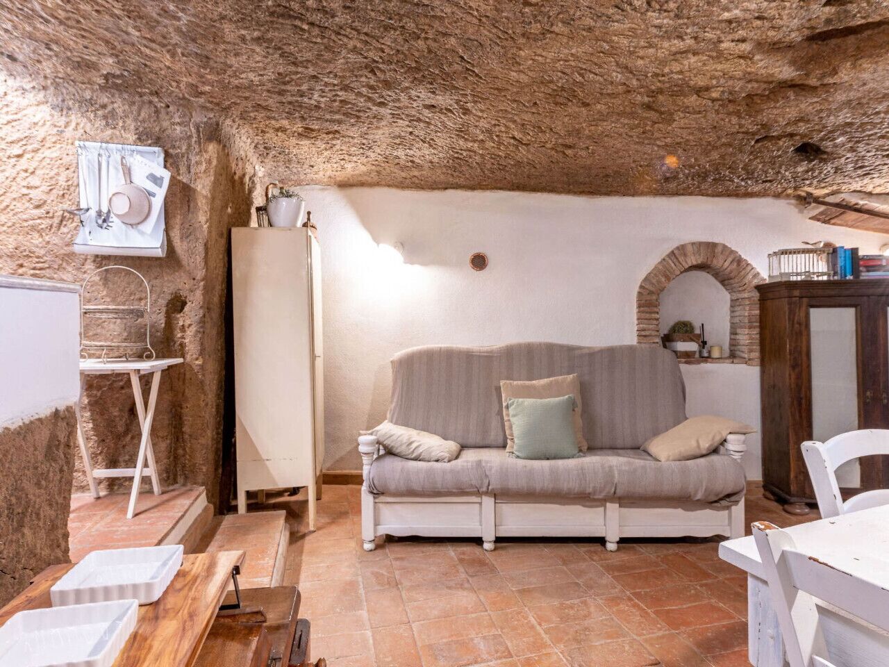 Un ambiente rustico con soffitto in pietra, un divano bianco, un tavolino e una parete in mattoni.