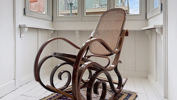 A rocking chair in a room with white walls and a view of buildings through large windows. - Maison No Catiau - De Panne (De Panne)