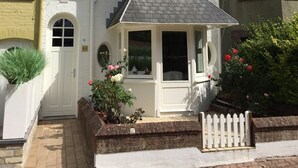 A two-story house with a white facade, a front door, and a small porch with a white picket fence. - Maison No Catiau - De Panne (De Panne)