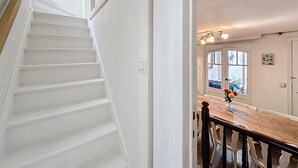 A staircase leading to a dining area with a wooden table and chairs, a window with a view, and a door with a light switch. - Maison No Catiau - De Panne (De Panne)