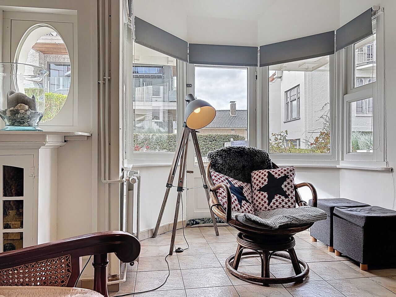 Ein Eckzimmer mit großem Fenster, einem Stativ, einem Schaukelstuhl und einem kleinen Tisch.