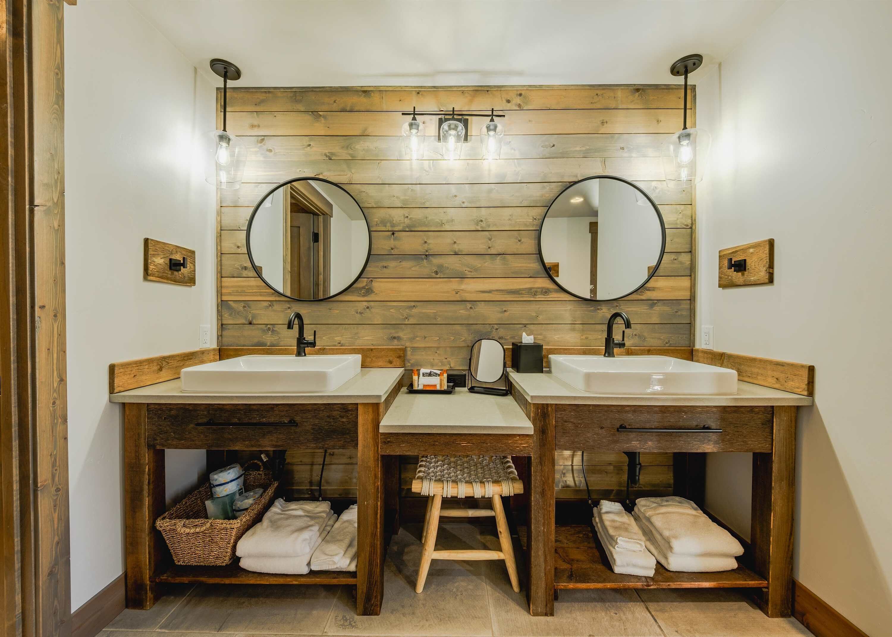A bathroom with two sinks, wooden wall paneling, and a mirror above each sink.