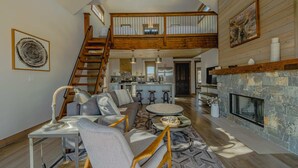 Un vaste espace de vie avec une chambre en mezzanine, une cheminée et une cuisine à l’arrière-plan.