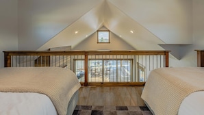 Une chambre avec deux lits, une rambarde en bois, une vue sur l’extérieur et un plafond en pente.