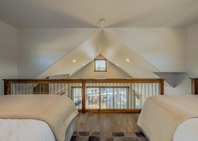 Un dormitorio con dos camas, baranda de madera, vistas al exterior y techo inclinado.