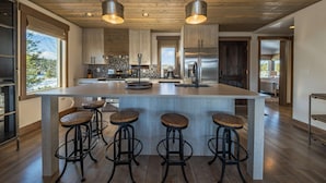 Une cuisine moderne dotée d’un grand îlot central, de tabourets de bar, d’appareils électroménagers en acier inoxydable et d’un plafond en bois.