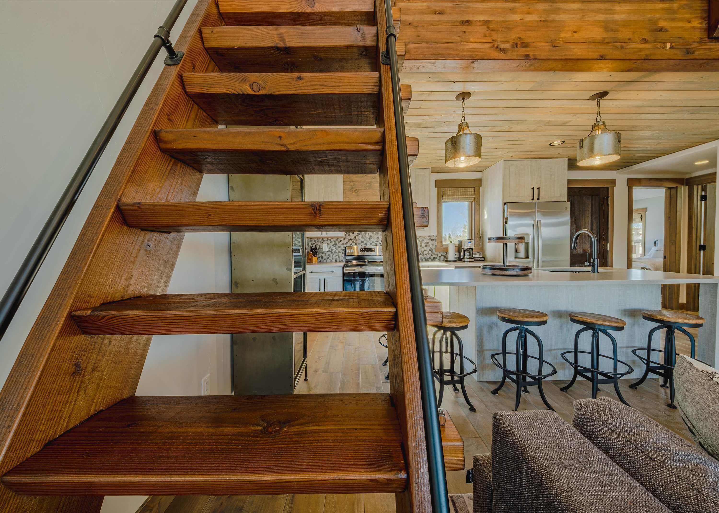 A wooden staircase leading to a kitchen with bar stools and a dining area.