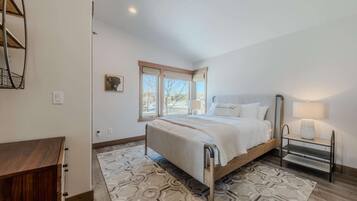 A bedroom with a bed, bedside table, lamp, and a window with a view.