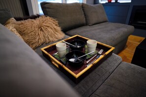 Un canapé gris avec un coussin moelleux marron, un plateau avec des tasses, un bol et des couverts.