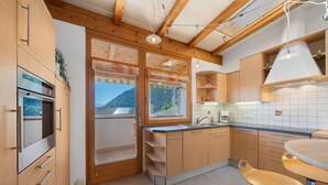 Een moderne keuken met houten kastjes, een inbouwoven, een groot raam en een barkruk.