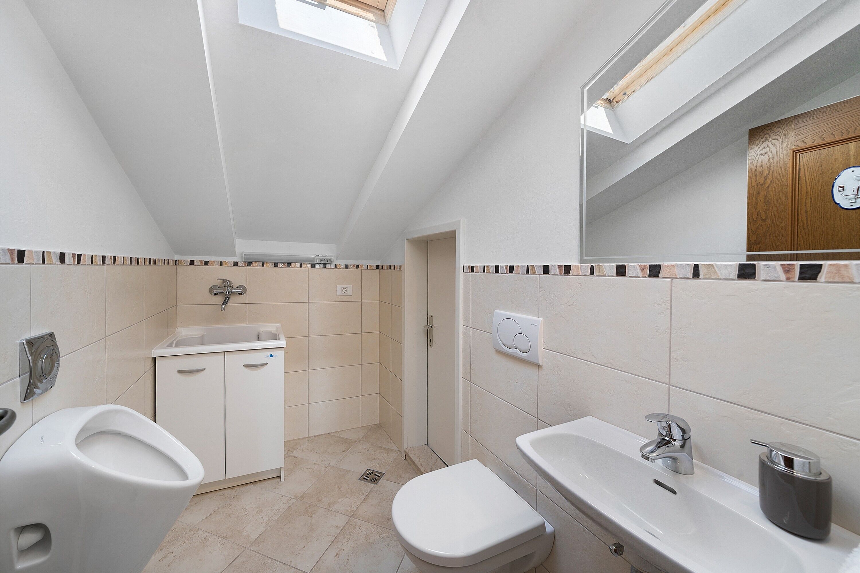 Een moderne badkamer met dakraam, toilet, wastafel en douche.