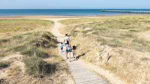 Un sentiero sabbioso che conduce a una spiaggia con un molo in lontananza.