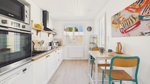 Cucina con mobili bianchi, piano cottura e forno a microonde. Si vede una finestra con vista sul verde.