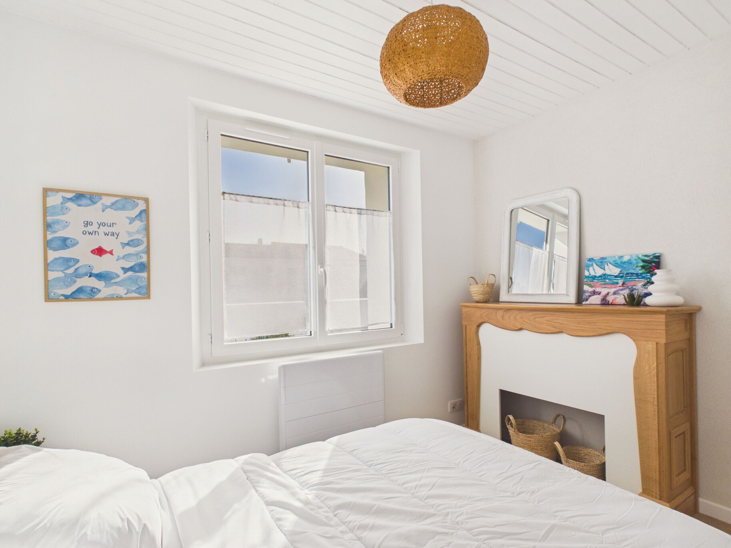 A bedroom with a bed, a window, a fireplace, and a wall with a framed picture.
