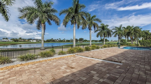A paved outdoor area with a swimming pool, palm trees, and a view of a golf course. - Stunning five-bedroom, 3 full bathroom home with views of lake and golf course (Marco Island)