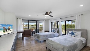 A hotel room with two beds, a desk, and a balcony with a view of the beach. - Stunning five-bedroom, 3 full bathroom home (Marco Island)