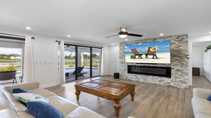 A living room with a stone fireplace, a ceiling fan, and a view of a pool and outdoor seating. - Stunning five-bedroom, 3 full bathroom home (Marco Island)