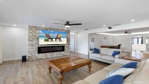 A living room with a stone wall, a flat-screen TV, a wooden coffee table, and a white sofa with blue cushions. - Stunning five-bedroom, 3 full bathroom home (Marco Island)