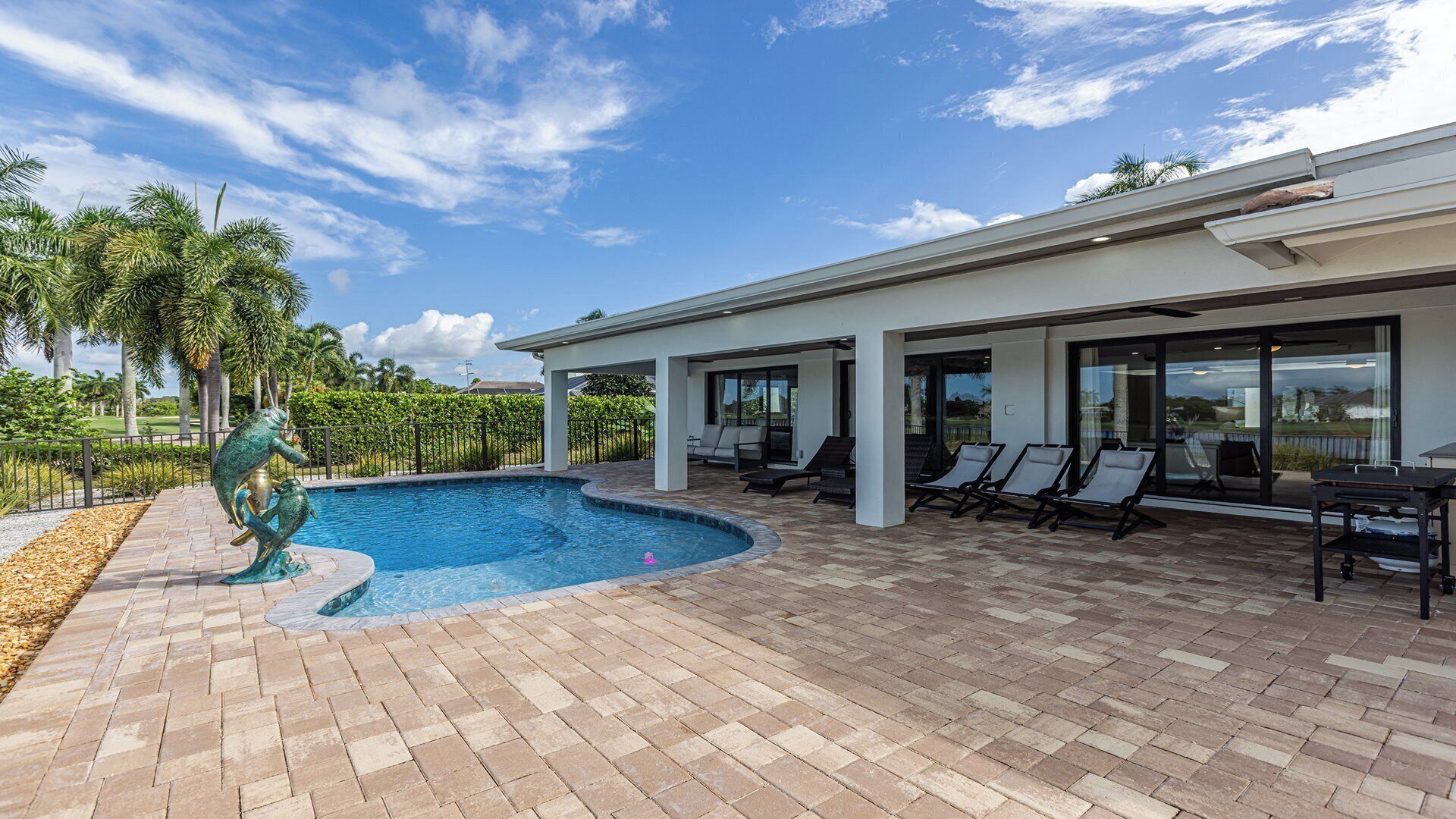 A swimming pool with a unique sculpture, a covered patio area with lounge chairs, and a view of the surrounding landscape.