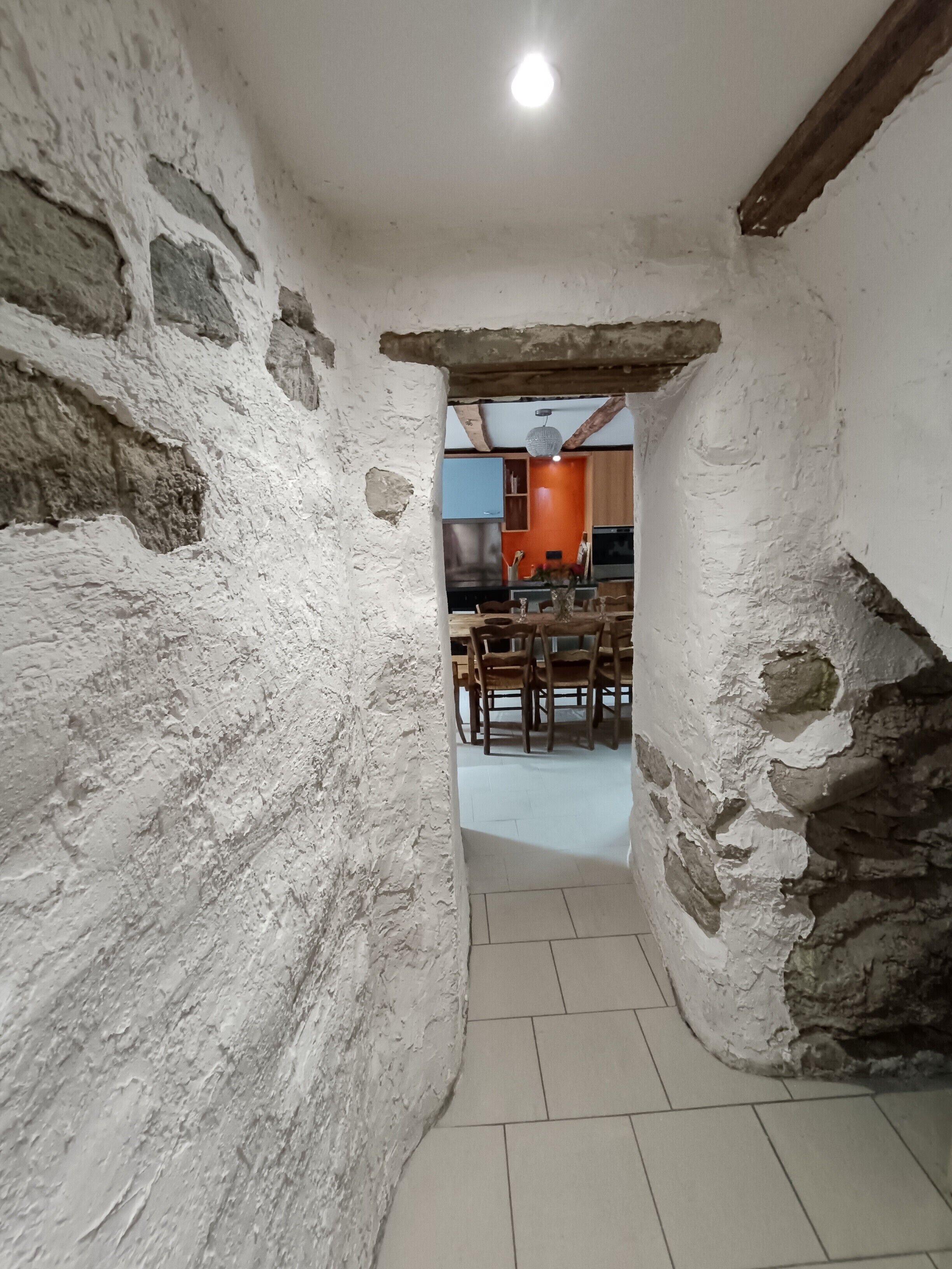 Un estrecho pasaje con paredes de piedra tosca que conduce a un comedor con muebles de madera y piso de baldosas.