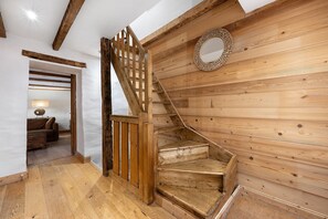 A wooden staircase with a circular mirror on the wall, a wooden floor, and a view into another room with a lamp and sofa.
