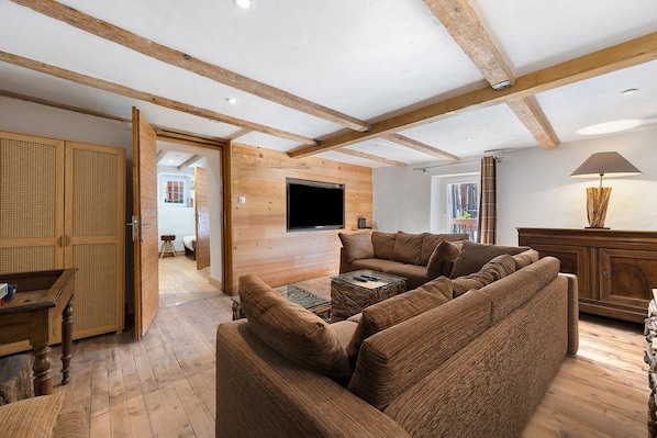 A spacious living area with a large sofa, wooden beams, a flat-screen TV, and a wooden cabinet.