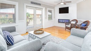 A living room with grey sofas, a white coffee table, a TV mounted on the wall, and ceiling fans. - Brass Rail 310 | Pool View Balcony, Elevator, Close to Beach (Tybee Island)