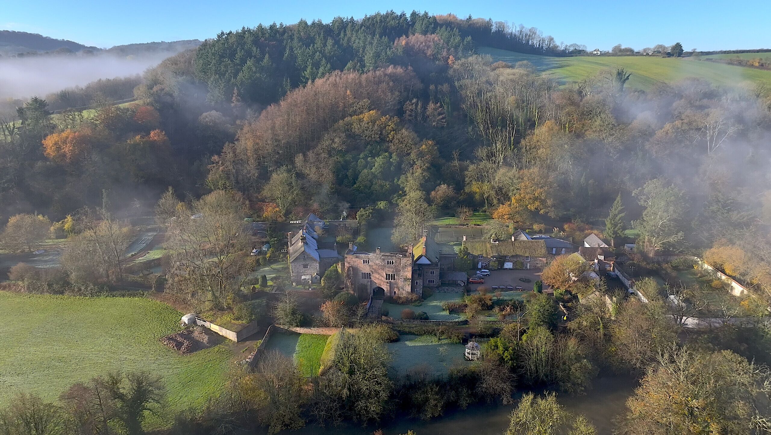 A historic estate with a central building surrounded by gardens and a small pond.