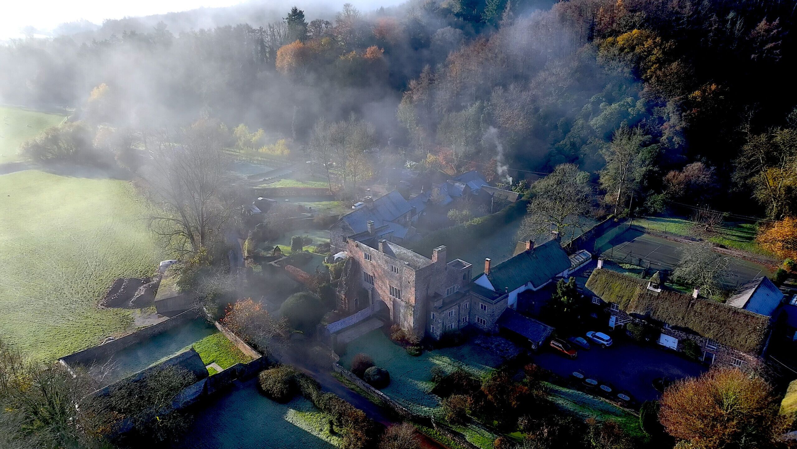 An aerial view of a historic estate with a large manor house, surrounding gardens, and a moat.