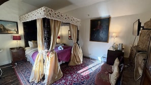 Camera da letto con letto a baldacchino, un quadro grande, un comodino, una lampada e un tappeto decorato.