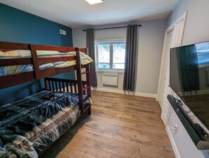 Une chambre avec des lits superposés, une télévision, une fenêtre avec des rideaux et un radiateur.