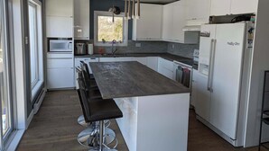 Una cocina moderna con armarios blancos, una isla central, electrodomésticos de acero inoxidable y un ventanal que aporta luz natural.