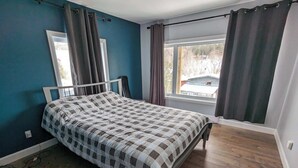 Un dormitorio con una cama, un ventanal con cortinas, vistas al exterior y una pared azul.