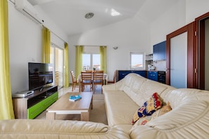 Ein Wohnzimmer mit einer Couch, Fernseher und einem Essbereich mit Stühlen und einem Tisch.