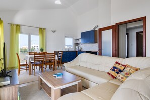 Ein Wohnzimmer mit Sofa, Couchtisch, Essbereich mit Stühlen und einer Küche mit blauen Schränken.