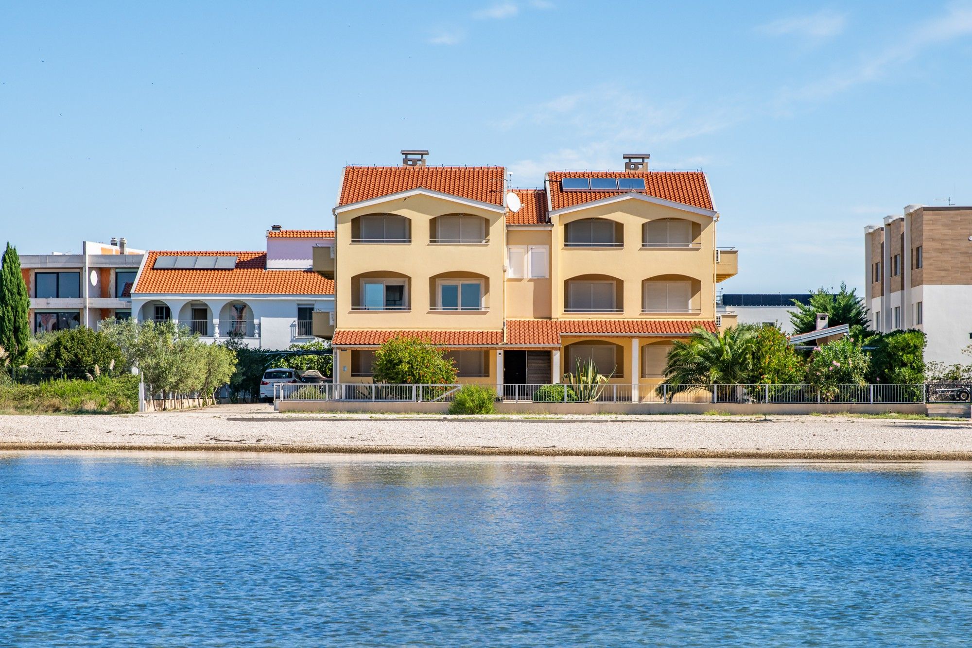 A multi-story building with a red-tiled roof, located near a body of water.