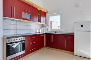 A kitchen with red cabinets, a white refrigerator, and a built-in oven. - Kotari Sukošan in Sukošan - Nord-Dalmatien / Kotari Sukošan in Sukošan - Appartement für 4 Personen AP4 (Sukosan)
