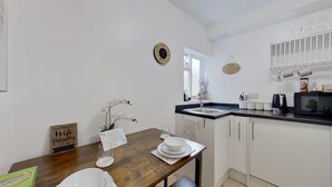 A kitchen with white cabinets, a wooden table, a white bowl, and a potted orchid. - Cosy 1 Bedroom Flat Near Balham Station (London)