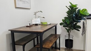 A dining area with a wooden table, benches, a potted plant, a clock, and a framed picture on the wall. - Cosy 1 Bedroom Flat Near Balham Station (London)