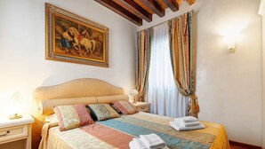 Une chambre à coucher avec un grand lit, une table de chevet, une lampe, un tableau accroché au mur et une fenêtre avec des rideaux.
