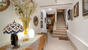 Un couloir avec un escalier, une table avec une lampe, un vase de fleurs et des œuvres d’art encadrées accrochées aux murs.