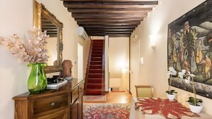 Un couloir avec un escalier en bois, un grand miroir, un vase vert et un tableau accroché au mur.