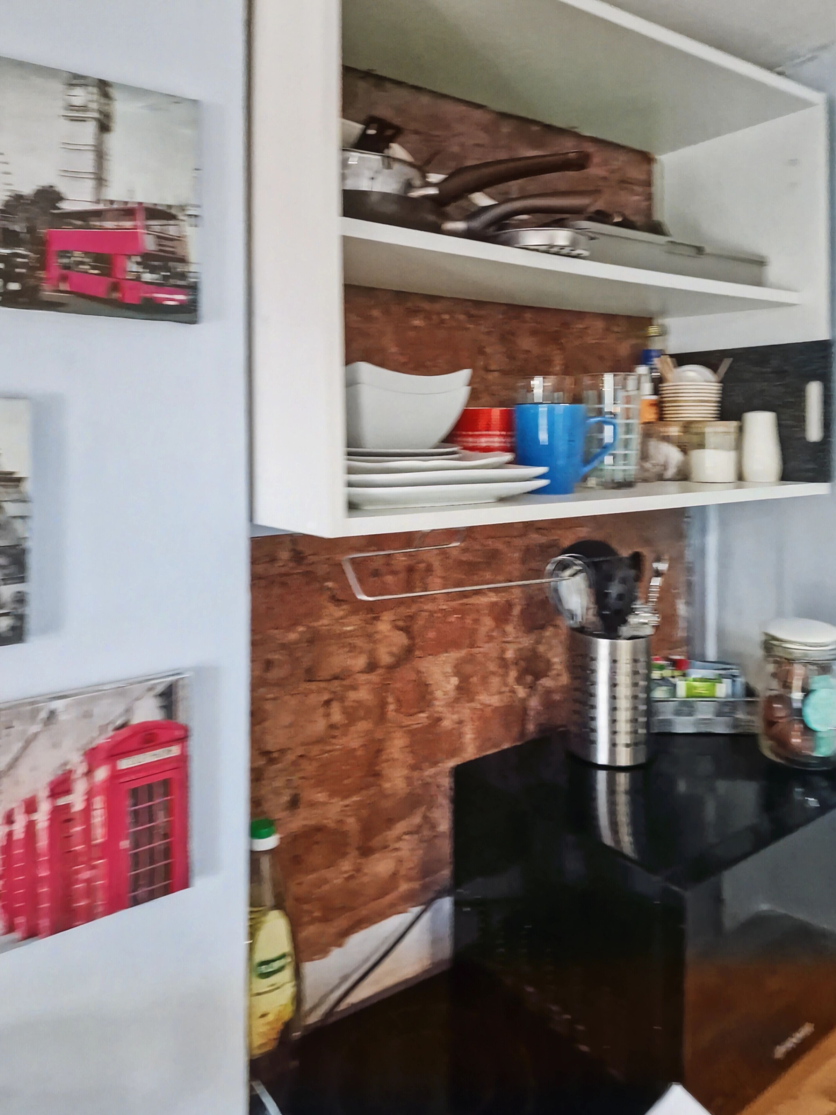 A kitchen with a black countertop, a stainless steel kettle, and various kitchen utensils.
